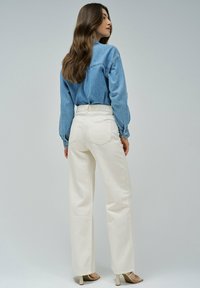 Camisa de denim azul claro de manga larga, combinada con pantalones anchos blancos de tiro alto y sandalias de tacón cuadrado beige.