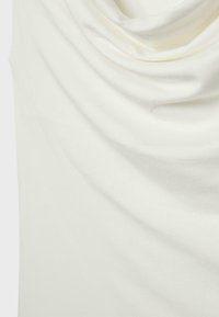 Soft, white fabric with gentle draped folds creating a smooth, flowing texture on a plain background.