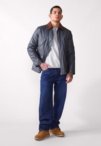Gray padded jacket with brown collar, gray sweatshirt, blue jeans, and brown boots. Jacket features pockets and a front zipper.