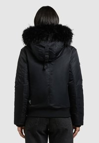 Geacă neagră tip puf cu glugă detașabilă din blană artificială, manșete cu nervuri și talie ajustabilă. Are un buzunar lateral și o textură netedă.