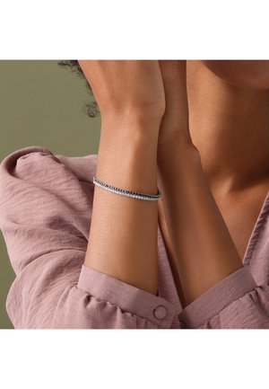 Zilverkleurige armband met afwisselende donkere en heldere kristalaccenten, gezet op een flexibele draad, gedragen om een pols tegen een zachte stoffen achtergrond.