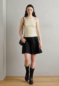 Débardeur côtelé crème avec des fines bretelles, associé à une jupe noire évasée. Accessoirisé avec un petit sac et des bottes noires à hauteur de genou.