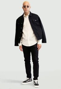 Black denim jacket, cream button-up shirt, black jeans, and black and white sneakers. Accessories include small sunglasses.