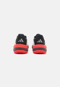 Svart och röda sportskor med meshtyg överdel, utrustade med en tjock röd mellansula, texturerad yttersula och tre-randigt logo på hälen.