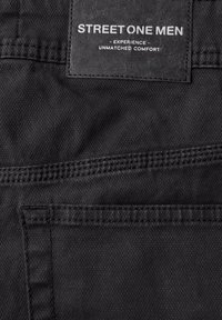 Zbliżenie na czarną tkaninę męską z naszytym kieszonką i metką z napisem "Street One Mężczyźni Doświadczają Niezrównanego Komfortu."