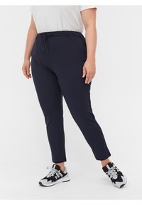 Marineblaue dehnbare Hose mit einem Kordelzugbund, schmalen Beinen und Seitentaschen, kombiniert mit schwarz-weißen Sport-Schuhen.
