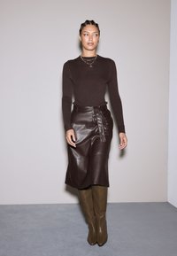 Ruskea ribbitetty pitkähiha toppi yhdistettynä ruskeaan nahkamidi-hameeseen, jossa on solmittava vyö. Vihreät polven yli ulottuvat tiukat saappaat viimeistelevät asun.