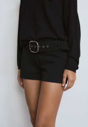 Black shorts made from a smooth fabric, fitted design, and a wide waistband with a large square silver belt buckle and eyelet details.