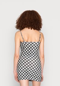 Vestido de xadrez gingham preto e branco com alças finas, design ajustado e comprimento acima do joelho, apresentando uma textura de tecido suave.