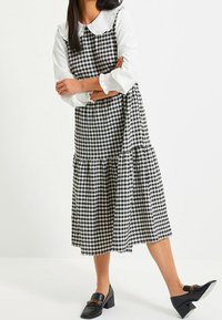 Svartvit rutig klänning med ett volangkrage, flerlagrad kjol och långa ärmar, tillsammans med svarta blockklackar.