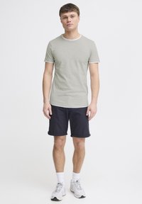 Tricou scurt cu mânecă scurtă de culoare verde deschis, cu un guler alb, asortat cu pantaloni scurți bleumarin. Modelul poartă șosete albe și teniși. Design minimal.