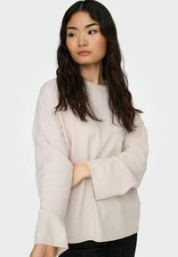 Suéter de manga larga beige claro con un ajuste holgado, escote redondo y puños acanalados. Textura suave con un detalle de costura mínima en el dobladillo.