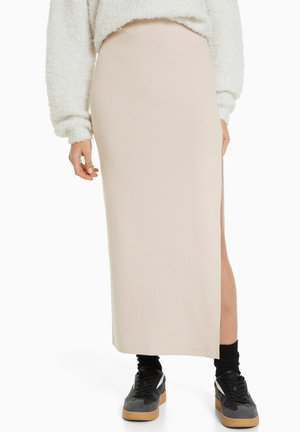 Beige midi-nederdel med sideslip sammen med sorte sokker, sorte sneakers og en hvid, blød langærmet top.