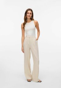 Lichtbeige, high-waisted, wijde gestreepte broek met zakken; gedragen met een aansluitend crèmekleurig tanktop en sandalen met open tenen.