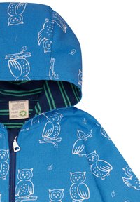 Giacca con cappuccio blu caratterizzata da un motivo di gufo bianco, chiusura con zip e rivestimento interno a strisce in blu scuro e verde. Realizzata con materiali biologici.
