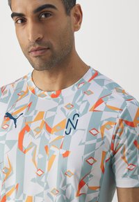 Camiseta atlética de manga corta con un patrón geométrico en tonos de blanco, azul claro, naranja y gris. Presenta el logo de PUMA y una textura suave.