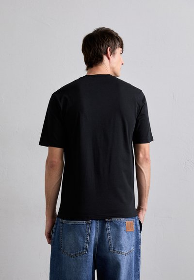 T-shirt en coton noir avec col rond, manches courtes et coupe décontractée, associé à un jean en denim bleu avec une patch en cuir marron.