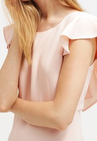 Šaty s krátkým rukávem v světle růžové tkanině s jemnou texturou; mají volánkové rukávy a kulatý výstřih.