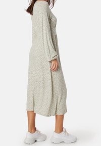 Lång, flödande klänning i ljusgrön med små rosa blommönster. Mjuk, lätt tyg, lång ärm och knälängd, matchad med vita sneakers.