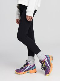 Leggings nere indossate con calzini grigi e scarpe da corsa multicolori con dettagli viola, turchese e arancione. Stile atletico confortevole.