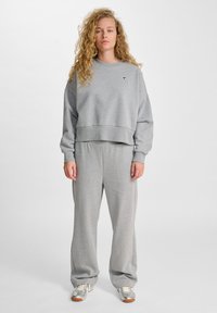 Felpa grigia cropped con scollatura rotonda e logo sul petto, abbinata a pantaloni della tuta grigi a vestibilità ampia. Texture in tessuto morbido.