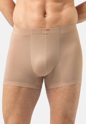 Mężczyzna noszący beżowe, teksturowane bokserki z wyprofilowanym pouch, stojący na jednolitym jasnym tle.