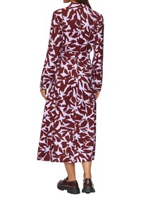 Długa bordowa sukienka z białym wzorem kwiatowym, z długimi rękawami, wcięciem w talii i zwiewną, długością sięgającą kostek spódnicą. Noszona z ciemnymi butami.