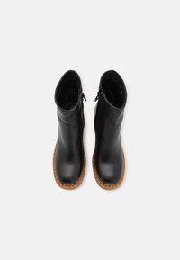 Botines de cuero negro con punta redonda, suela de goma ribeteada en color marrón claro y cremalleras laterales para facilitar su uso. Textura suave y diseño minimalista.