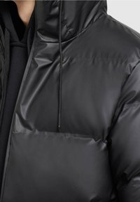 Schwarze Pufferjacke mit einer glatten, glänzenden Oberfläche. Verfügt über einen Reißverschluss vorne, eine verstellbare Kapuze und eine große Fronttasche.