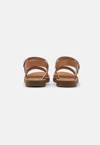 Brown flat sandals with three narrow straps and a buckle detail. Textured sole and smooth material, offering a minimalist design.