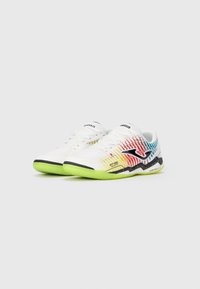 Witte sportschoenen met een gestructureerd oppervlak; kleurrijk verlooppatroon in rood, geel en blauw; groene buitenzool; zwarte accenten en logo.