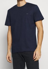 Short-sleeve navy blue cotton t-shirt with a crew neck and small logo on the left chest. Features a simple, textured finish.