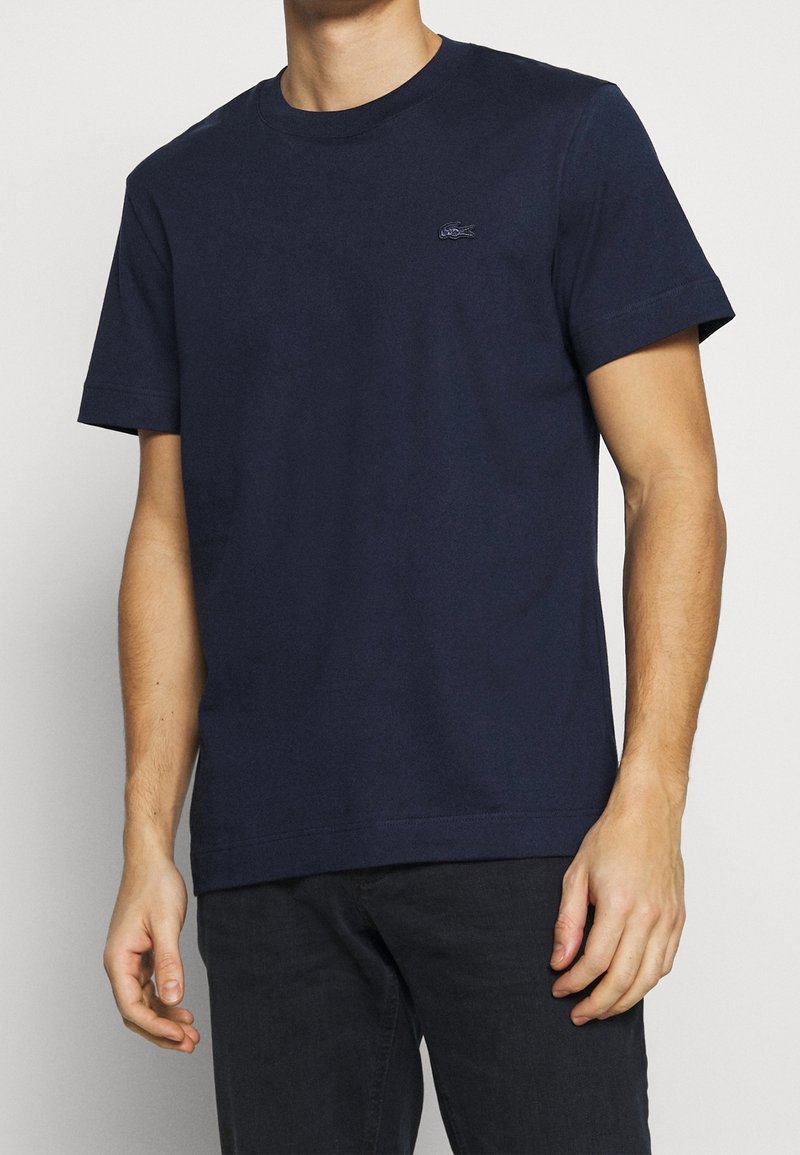 Short-sleeve navy blue cotton t-shirt with a crew neck and small logo on the left chest. Features a simple, textured finish.