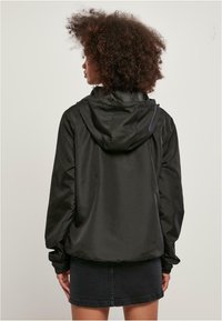Zwarte capuchonjack met een gladde, glanzende textuur, elastische boorden en een losse pasvorm, gecombineerd met een denim rok.