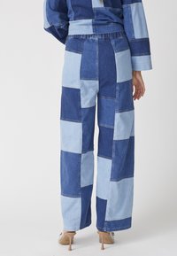 Mikiny denim nohavice s patchworkom, ktoré kombinujú tmavomodré a svetlomodré odtiene, široké nohavice a elastický pás.