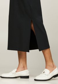 Zwart midi-jurk met zijsplit, gecombineerd met witte leren loafers met geperforeerde details en een zwarte zool.
