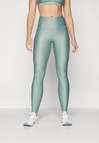 Leggings a vita alta di colore verde acqua realizzati in un tessuto liscio e elasticizzato; presentano un logo sulla coscia e si abbinano a un reggiseno sportivo coordinato.