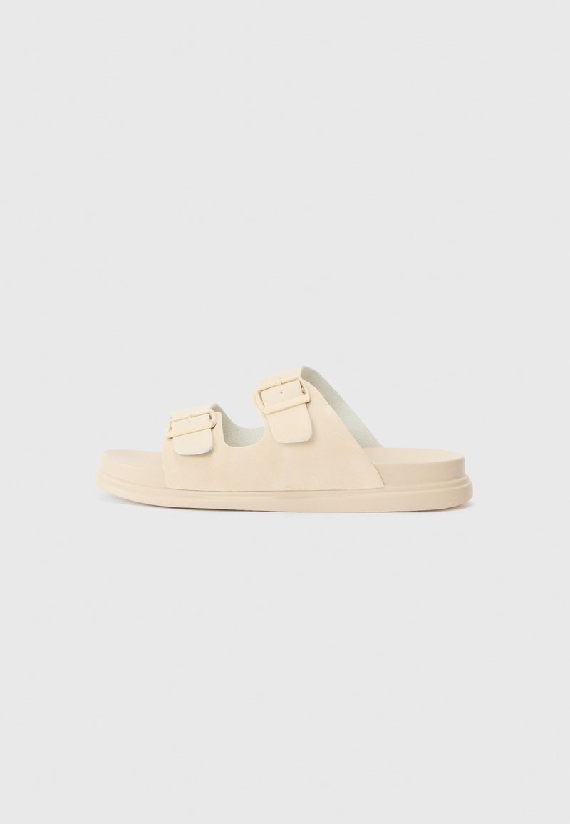 Beige slide sandals with two adjustable straps, smooth suede material, and a thick sole for cushioning. Minimalistic design, open toe.