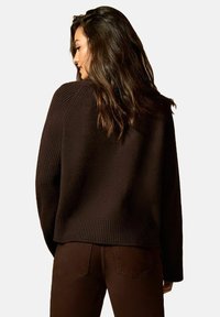 Pull marron côtelé avec une coupe décontractée, présentant un col large et un corps texturé. Associé à un jean foncé ajusté.