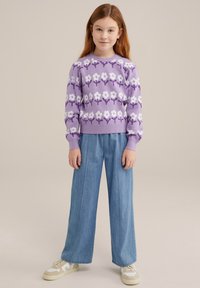 Pulover violet cu model floral, asociat cu pantaloni denim largi și adidași albi. Puloverul are un decolteu rotund și manșete cu jerse. 
