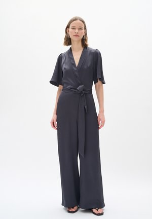 Jupe-pantalon gris avec des manches courtes, décolleté en V profond, ceinture à la taille, jambes larges et texture de tissu lisse. Accentué par un design minimaliste.