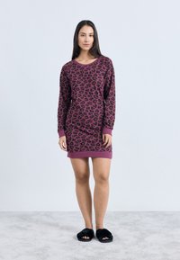 Obleka z leopardjim potiskom v vijolični in črni barvi, z dolgimi rokavi in zaobljenim izrezom, z rebrastimi manšetami in robom. Nošena s črnimi copati.