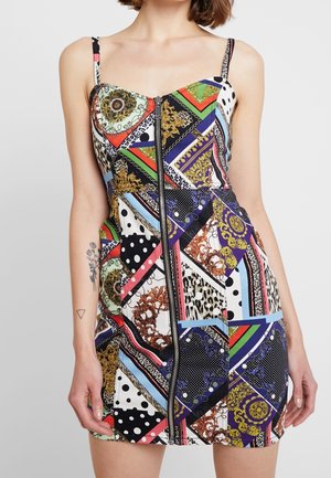 Femme portant une robe patchwork sans manches multicolore avec une fermeture éclair à l'avant, des motifs géométriques et animaliers, et des bretelles fines.