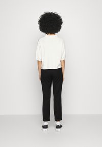 Suéter blanco corto, pantalones negros ajustados, zapatillas en blanco y negro. Modelo visto desde atrás, con cabello rizado y sin accesorios visibles.