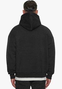 Svart hettegenser laget av myk stoff, med stor hette, senkede skuldersømmer og ribbede mansjetter og nederkant. Enkel, ensfarget design.