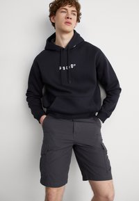 Sudadera negra con logo blanco, que cuenta con un bolsillo canguro y cordón. Pantalones cortos de carga grises con bolsillos laterales y un ajuste relajado.