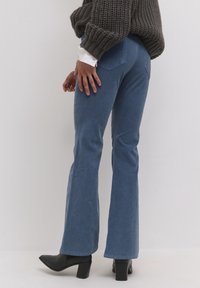 Vaqueros acampanados azul claro con textura suave, que cuentan con bolsillos traseros y un ligero elastán. Combinados con un suéter de punto gris grueso y botas negras de tacón.