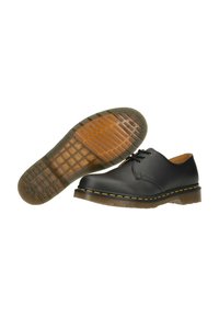 Scarpe in pelle nera con punta arrotondata, cuciture gialle e una suola in gomma spessa caratterizzata da un motivo testurizzato e bordi arrotondati.