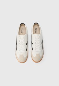 White and black vegan sneakers featuring smooth leather and suede textures, lace-up closure, and a tan rubber sole.