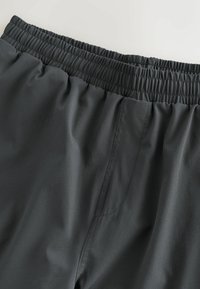 Donkergrijze sportshorts met een elastische tailleband, voorzien van soepel stof en een zijzak. Geen zichtbare patronen of hardware details.